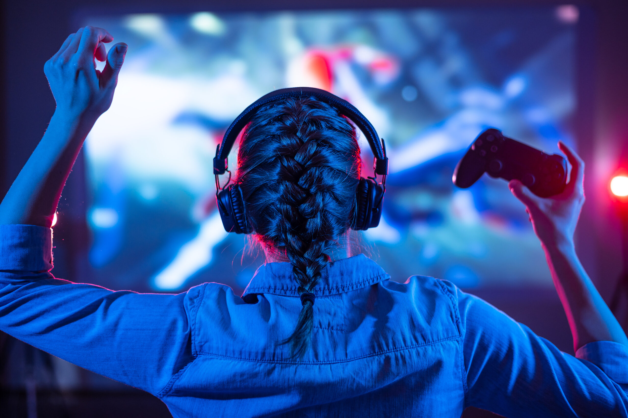 Ung person foran en stor skjerm, holder en gamingkontroller.
