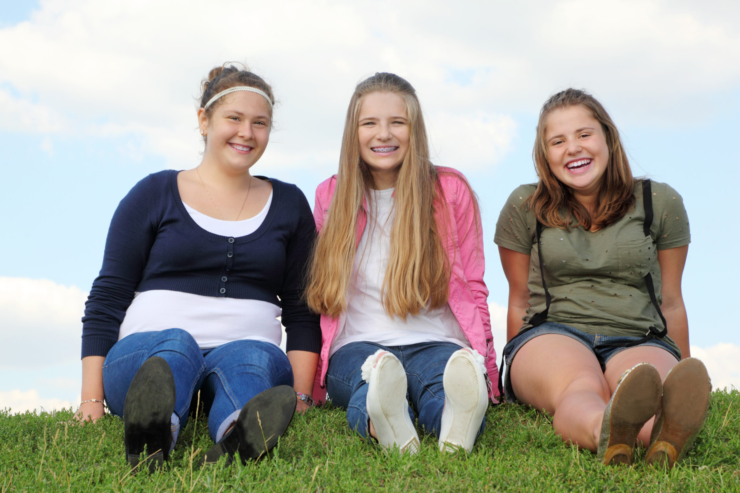 Tre galde jenter sitter på gresset.