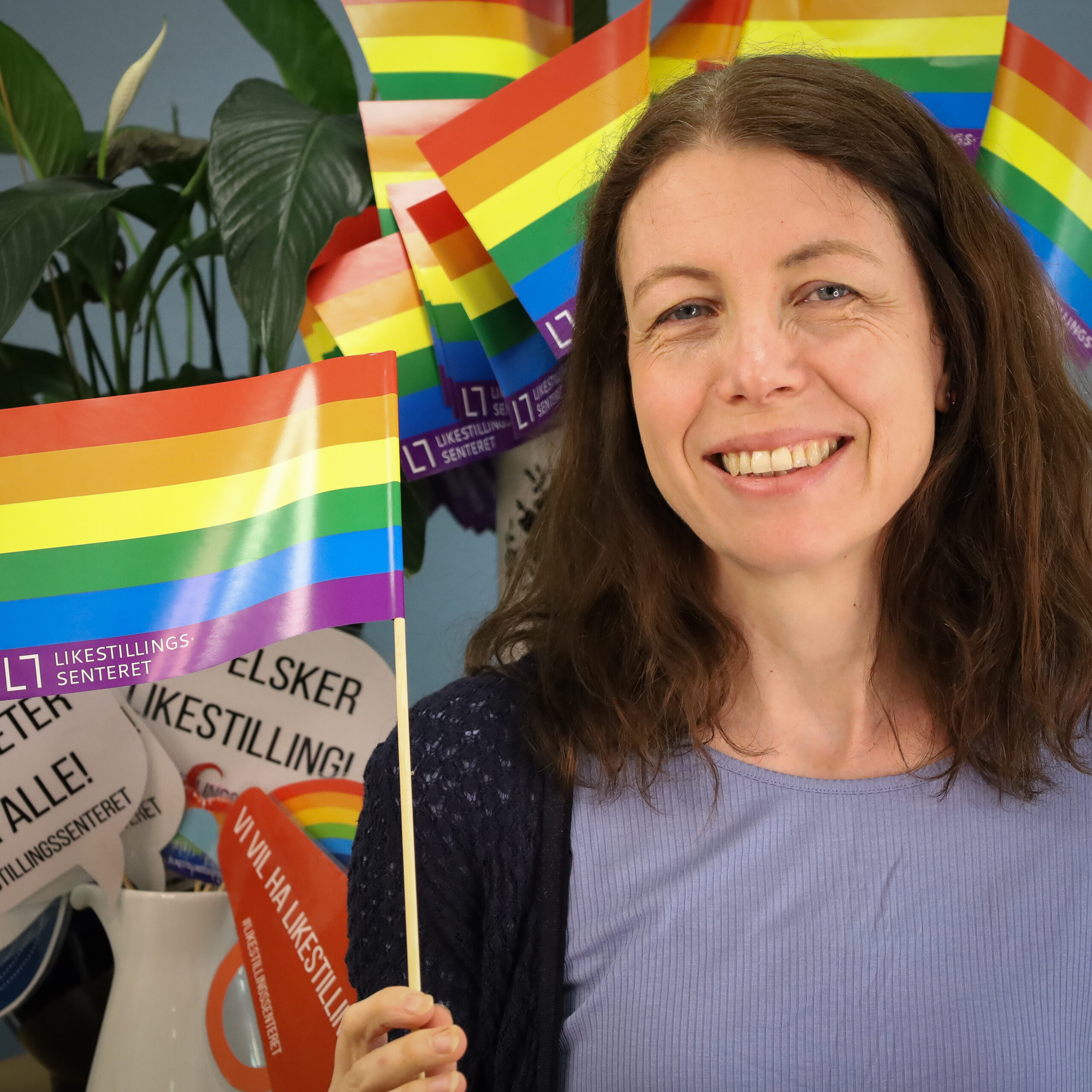 Mona holder et regnbueflagg med Likestillingssenterets logo på.