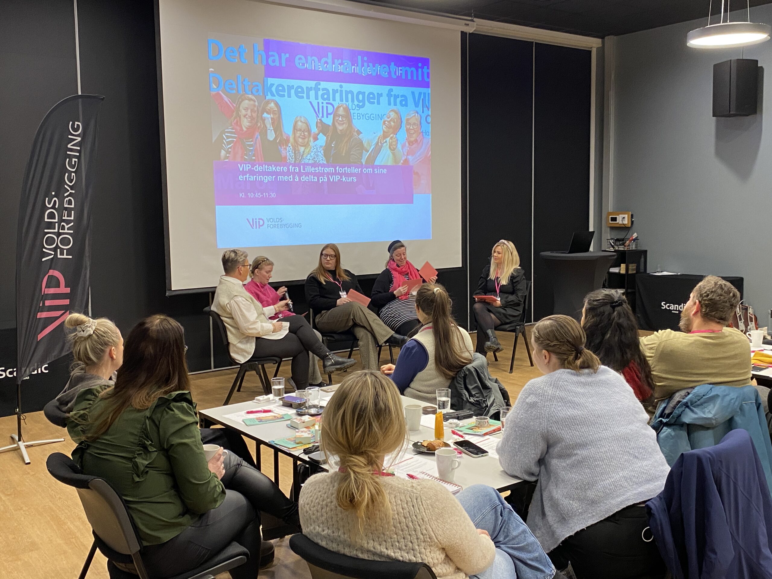 En forsamling hører på en gruppe mennesker snakke fra scenen.