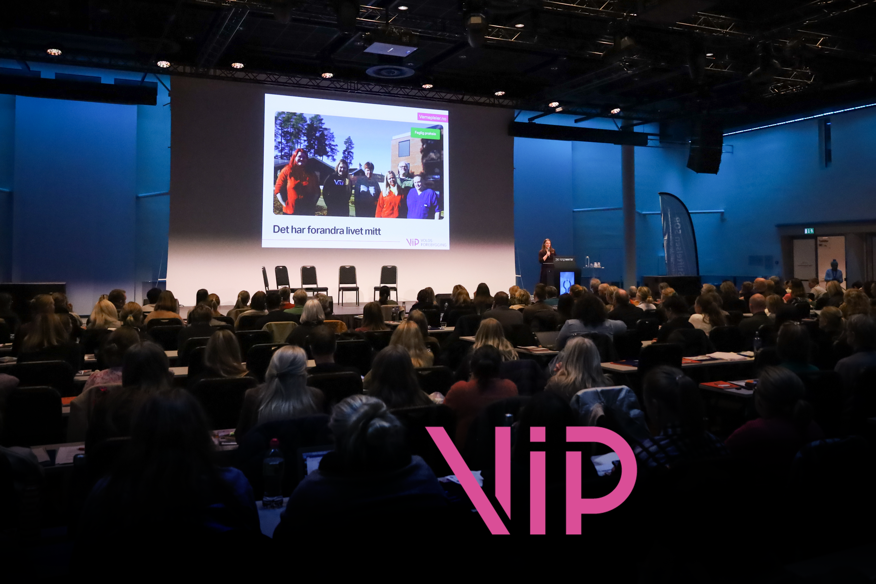 Forsamling foran en presentasjon av VIP. Bokstavene VIP står i rosa foran i bildet.