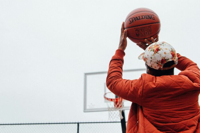 En gutt i oransje jakke kaster en basketball. Været er tåkete.