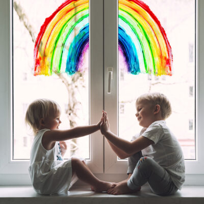 To små barn leker foran et vindu som har en tegning av en regnbue.