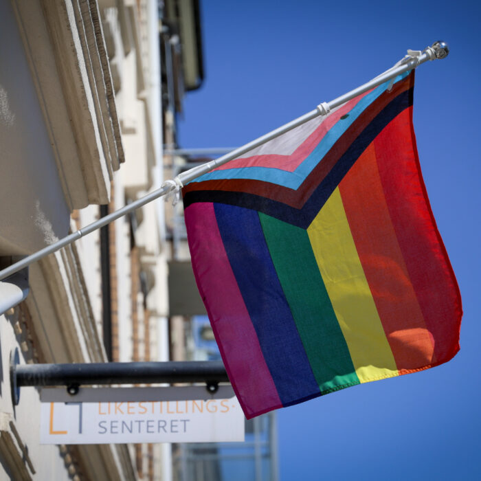Det progressive pride-flagget henger foran skilt med Likestillingssenteret-logo.