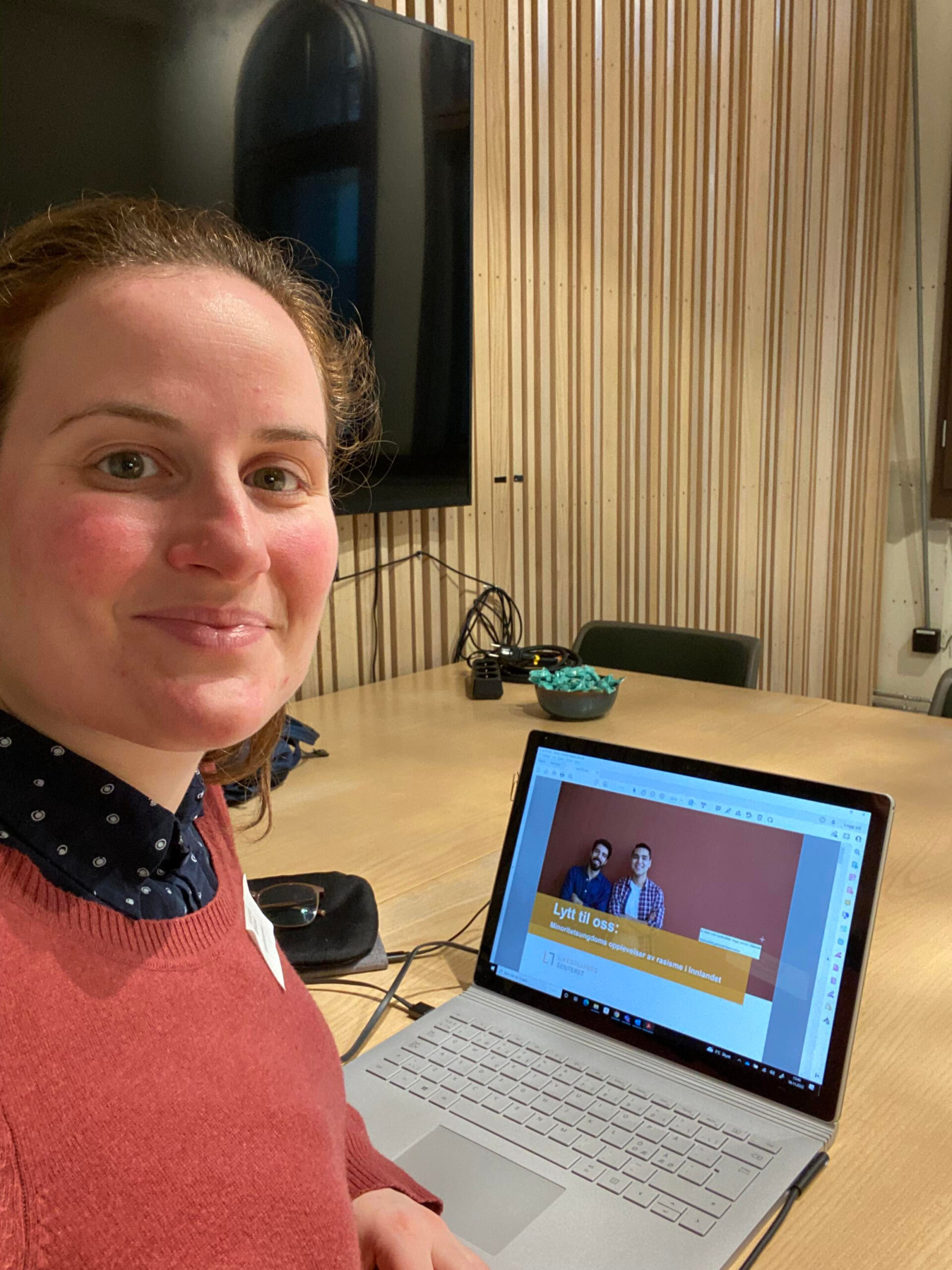 Kristina Miklavic sitter ved en laptop i et radiostudio. Hun ser i kamera og smiler.