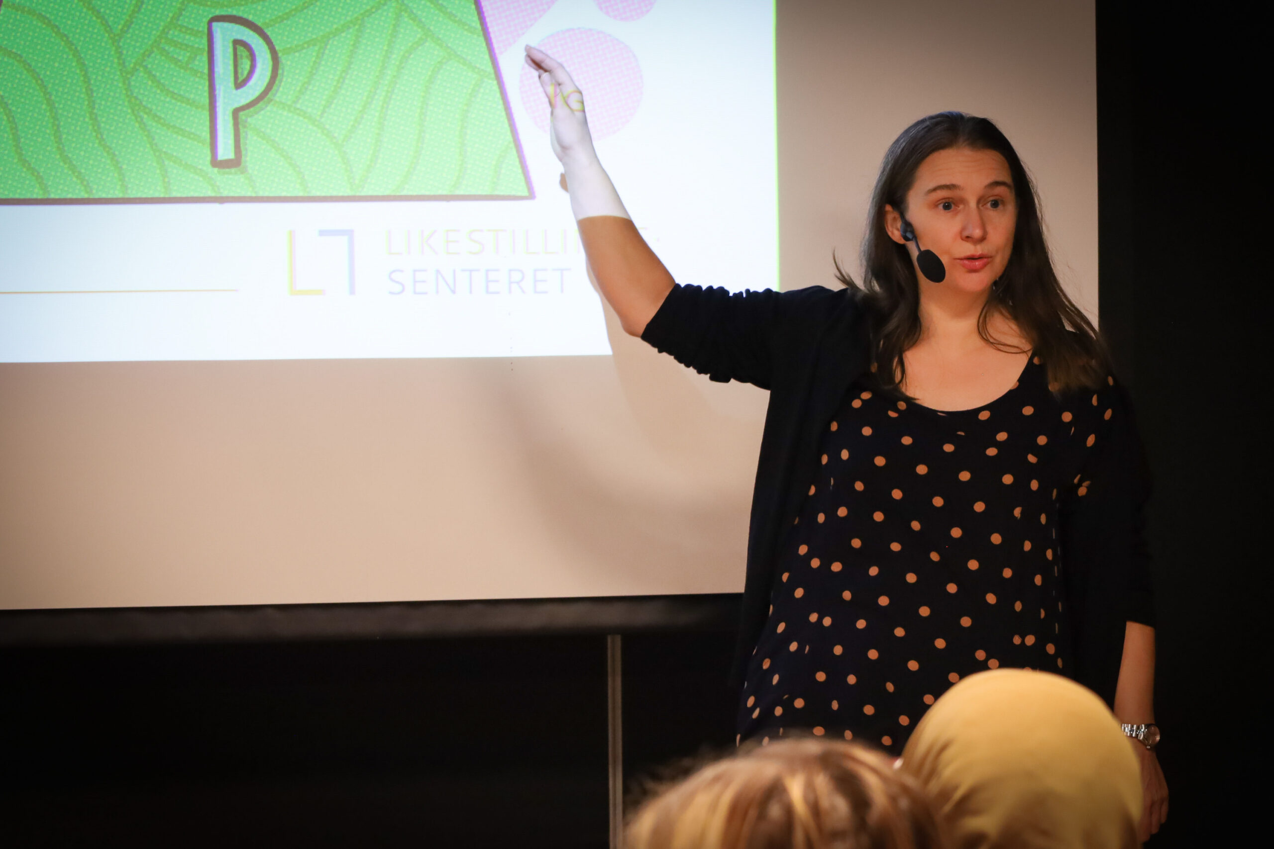 Frøydis Sund holder foredrag. På veggen bak henne er en skjerm med en presentasjon.