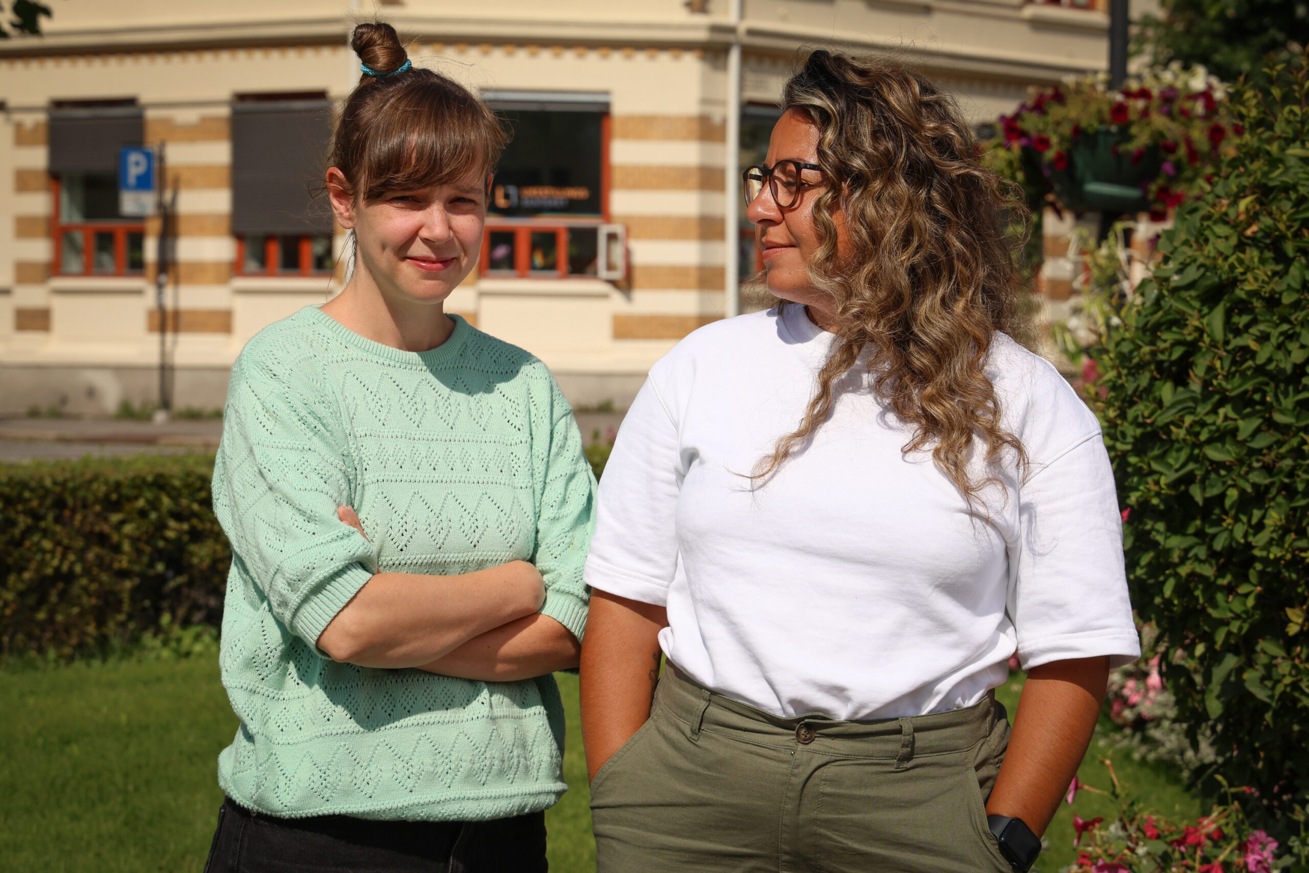 Silje og Hasti står utenfor kontoret til Likestillingssentret. SIlje står med armene i kors og ser i kamera. Hasti står med henda i lomma og ser på Silije.