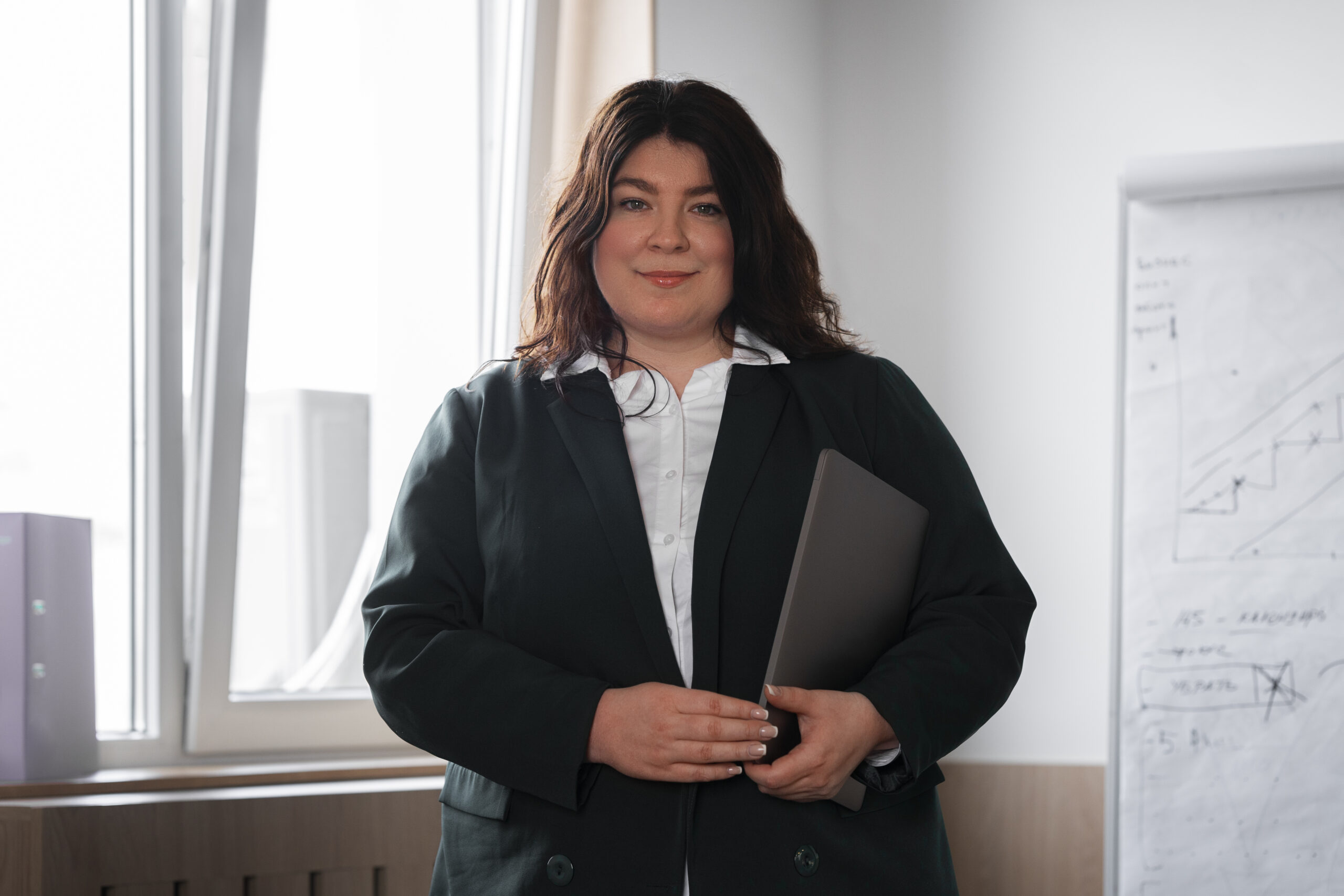 En person står med en laptop i hendene. Smiler og ser i kamera.