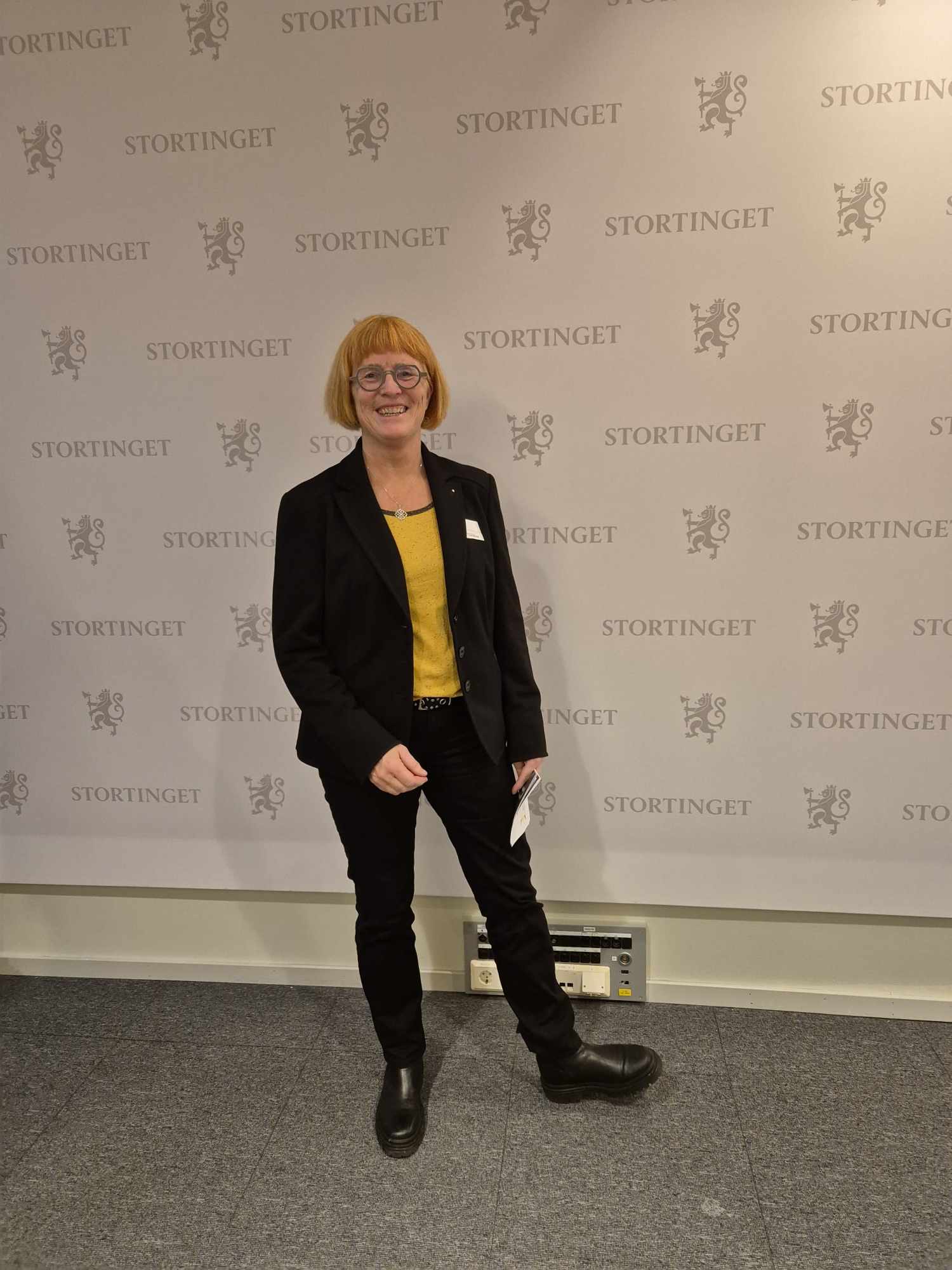 Goro Ree-Lindstad står foran en vegg tapetsert med Stortingets logo.