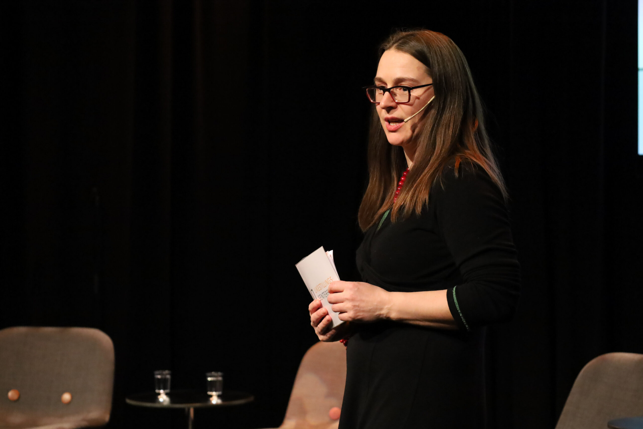 Frøydis Sund på scena, hun har mikrofon og holder talekort.