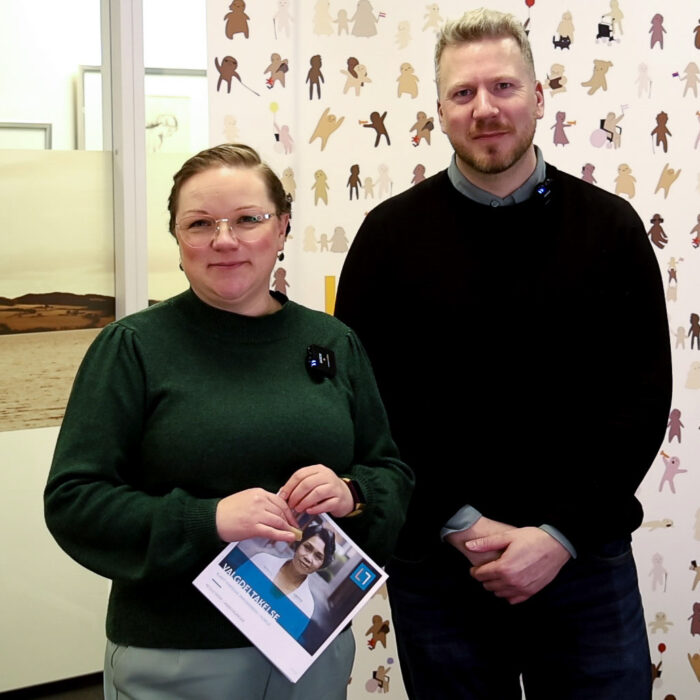 Annette og Eirik står ved siden av hverandre og ser i kamera. Annette holder en brosjyre.