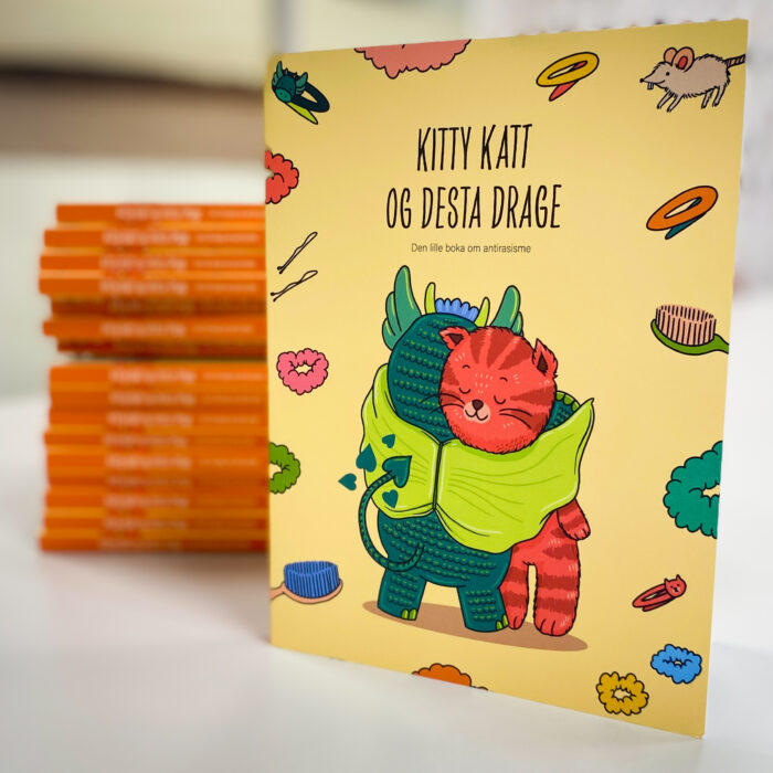Bilde av omslaget til boka Kitty Katt og Desta Drage - den lille boka om antirasisme. En rød katt og en grønn drage klemmer hverandre.
