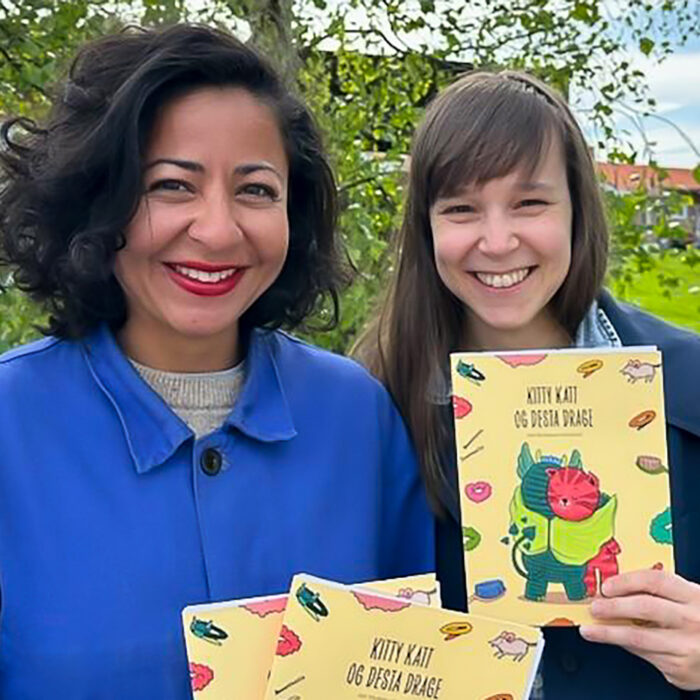 Nina og Silje holder opp hver sin bok. Begge ser i kamera og smiler.