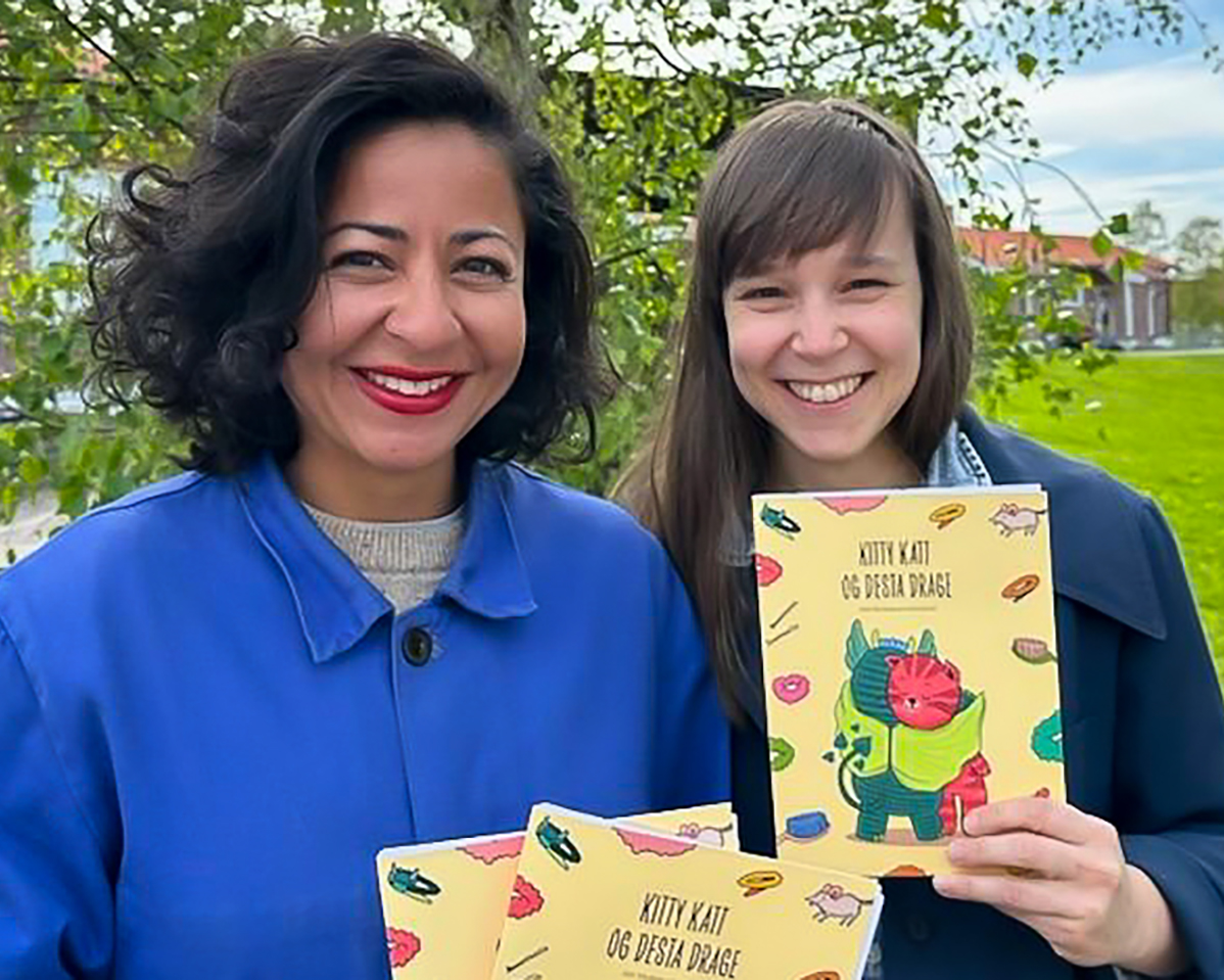 Nina og Silje holder opp hver sin bok. Begge ser i kamera og smiler.