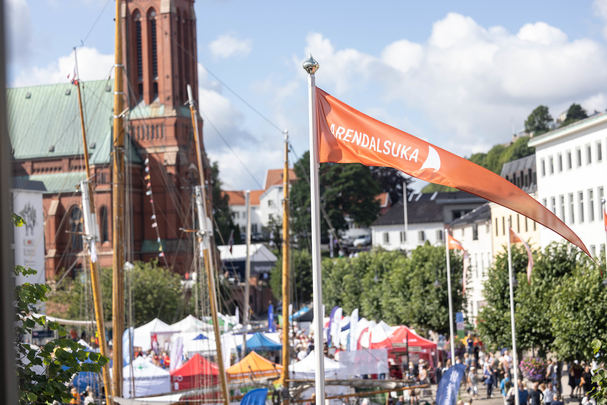 Et oransje banner med teksten Arendalsuka vaier i vinden med byen i bakgrunn.