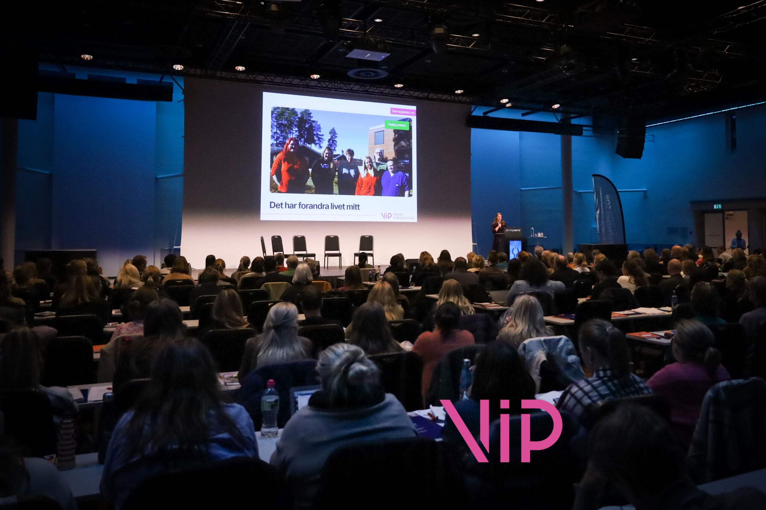 Publikum foran en storskjerm med bilde av en gjeng mennesker og teksten «Det har forandre livet mitt.»