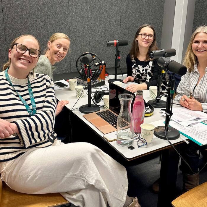 Fire personer sitter rundt et bord med mikrofoner. Alle ser i kamera.