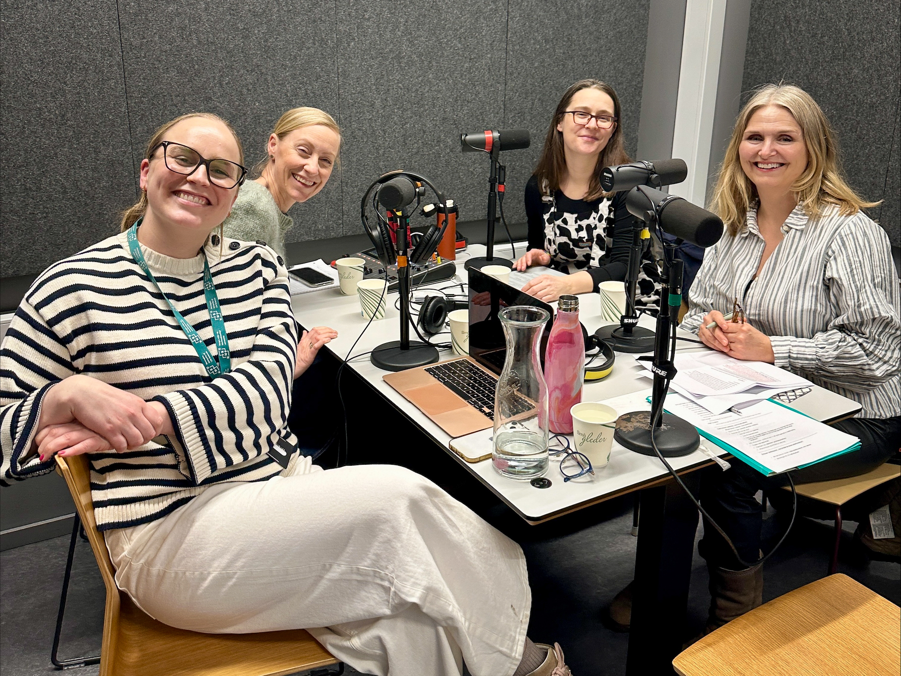 Fire personer sitter rundt et bord med mikrofoner. Alle ser i kamera.