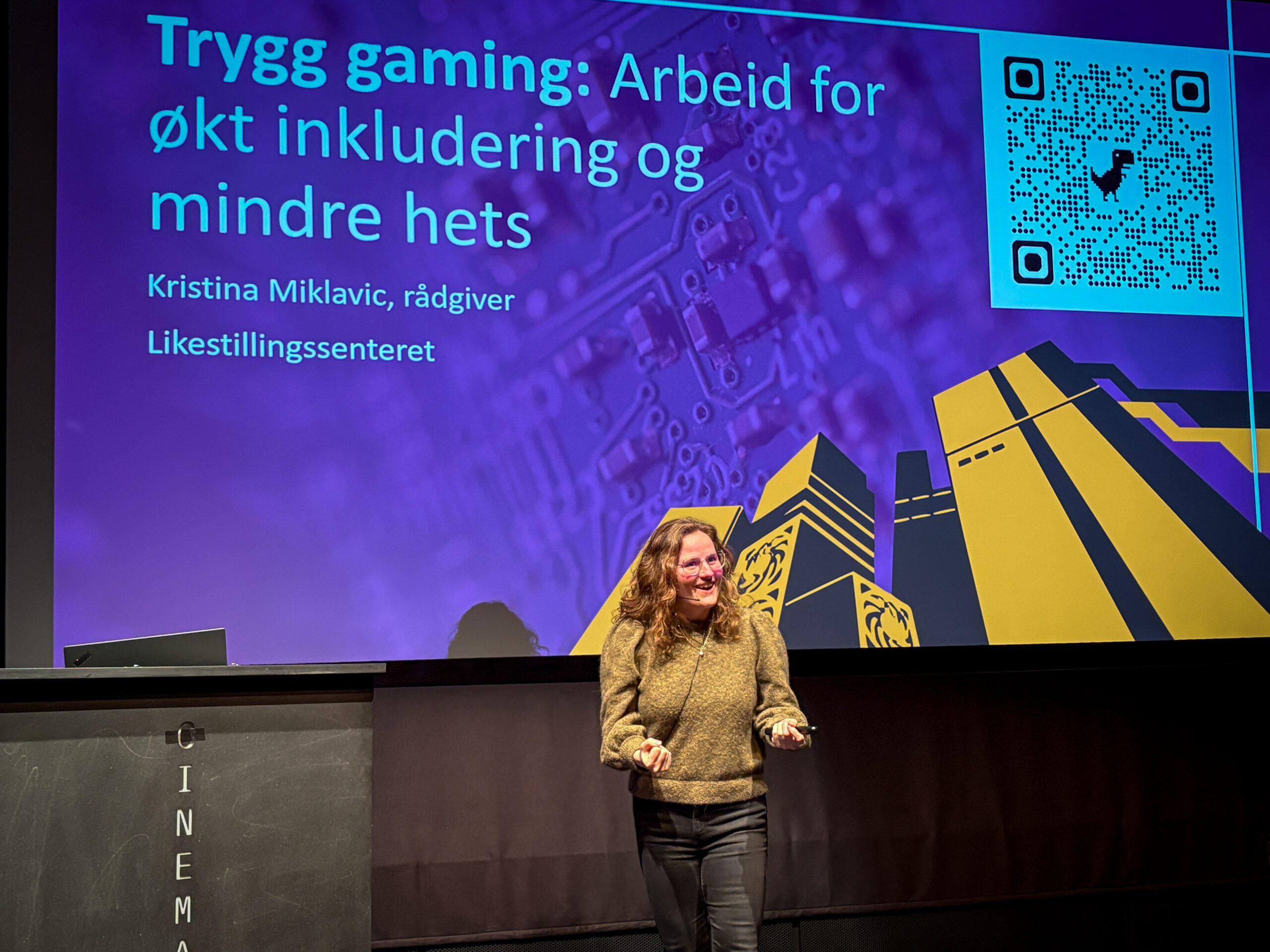 Kristina Miklavic på scenen for en presentasjon med teksten 'Trygg gaming: arbeid for økt inkludering og mindre hets'