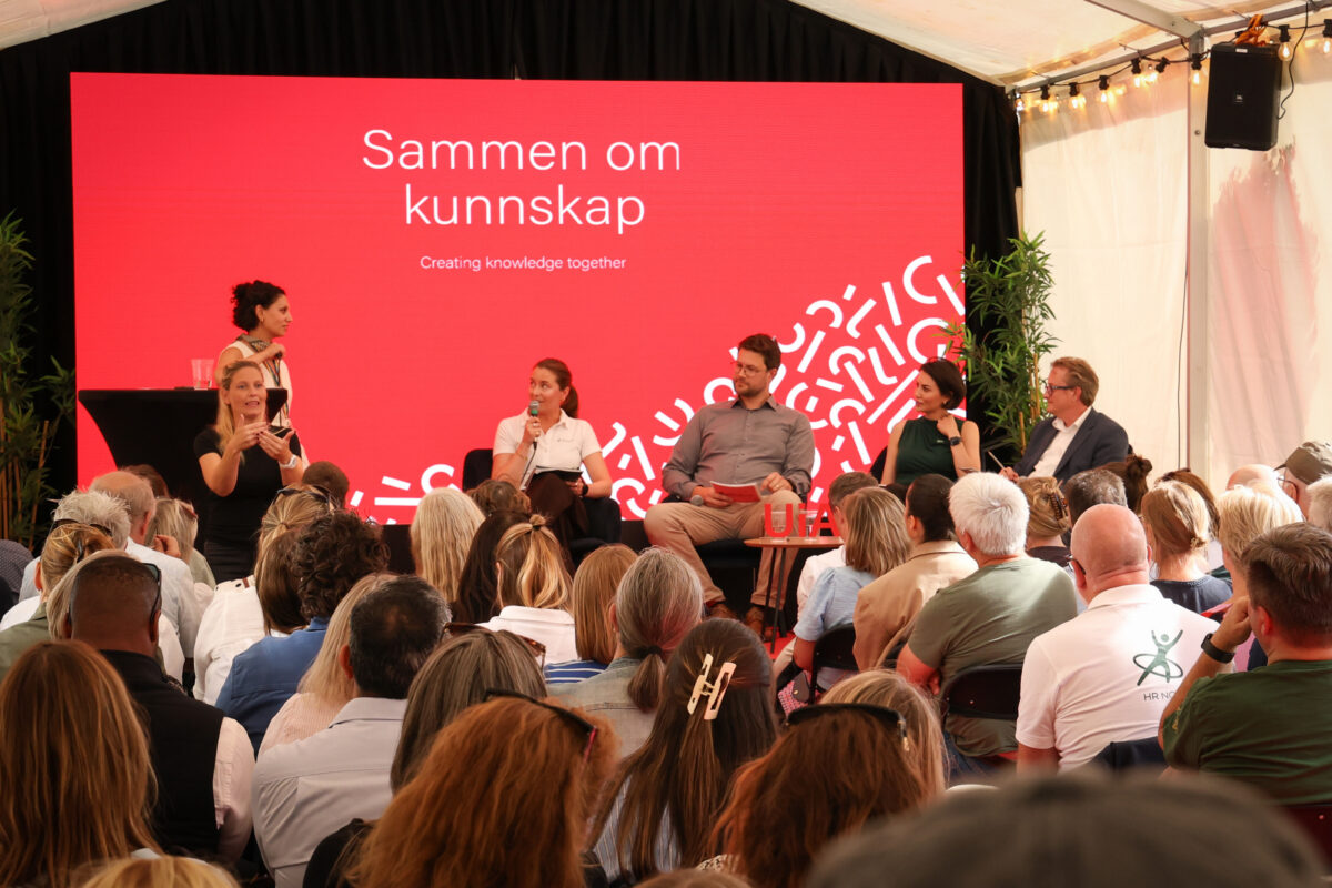 Scene med seks paneldeltakere foran et publikum.