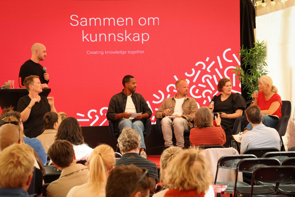 Scene med fem paneldeltakere foran et publikum.