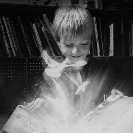 Et barn ser i en bok, det flyr fugler ut fra boka.