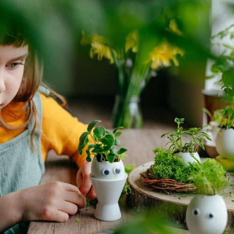 Little girl decorating eggshell with toy eyes on the table